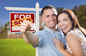 Mixed Race Excited Military Couple In Front of New Home with New House Keys and Sold Real Estate Sign Outside.